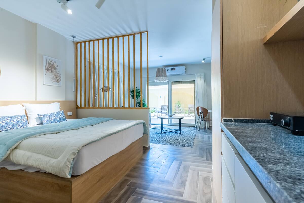 Une chambre moderne avec un lit en bois, une vue sur le balcon et un coin cuisine doté de plans de travail en granit.