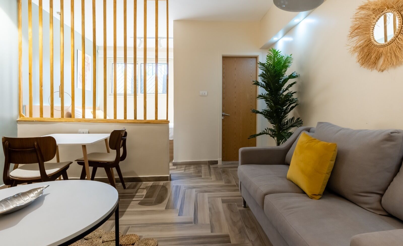 A living room with a sofa, a dining table with chairs, a potted plant, and a door.
