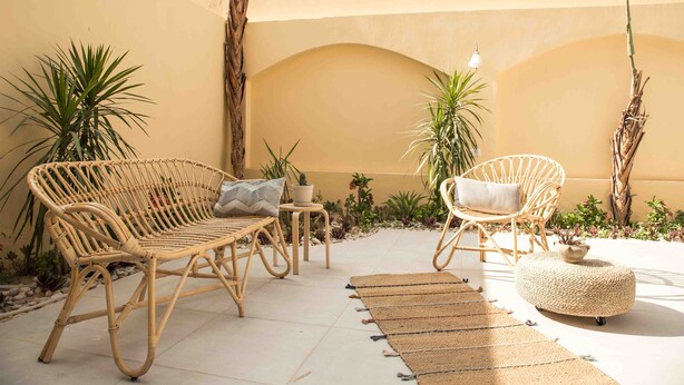 A sunlit patio with wicker furniture, a woven ottoman, and various plants. - Bird Nest Near Arkan Plaza  (Sheikh Zayed City)