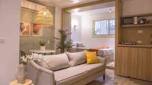 A modern living room with a sofa, a small table with a plant, and a hanging light fixture. - Bird Nest Near Arkan Plaza  (Sheikh Zayed City)