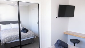 Une chambre d’hôtel moderne équipée d’un lit, d’un téléviseur à écran plat, d’une étagère en bois et d’un petit tabouret.