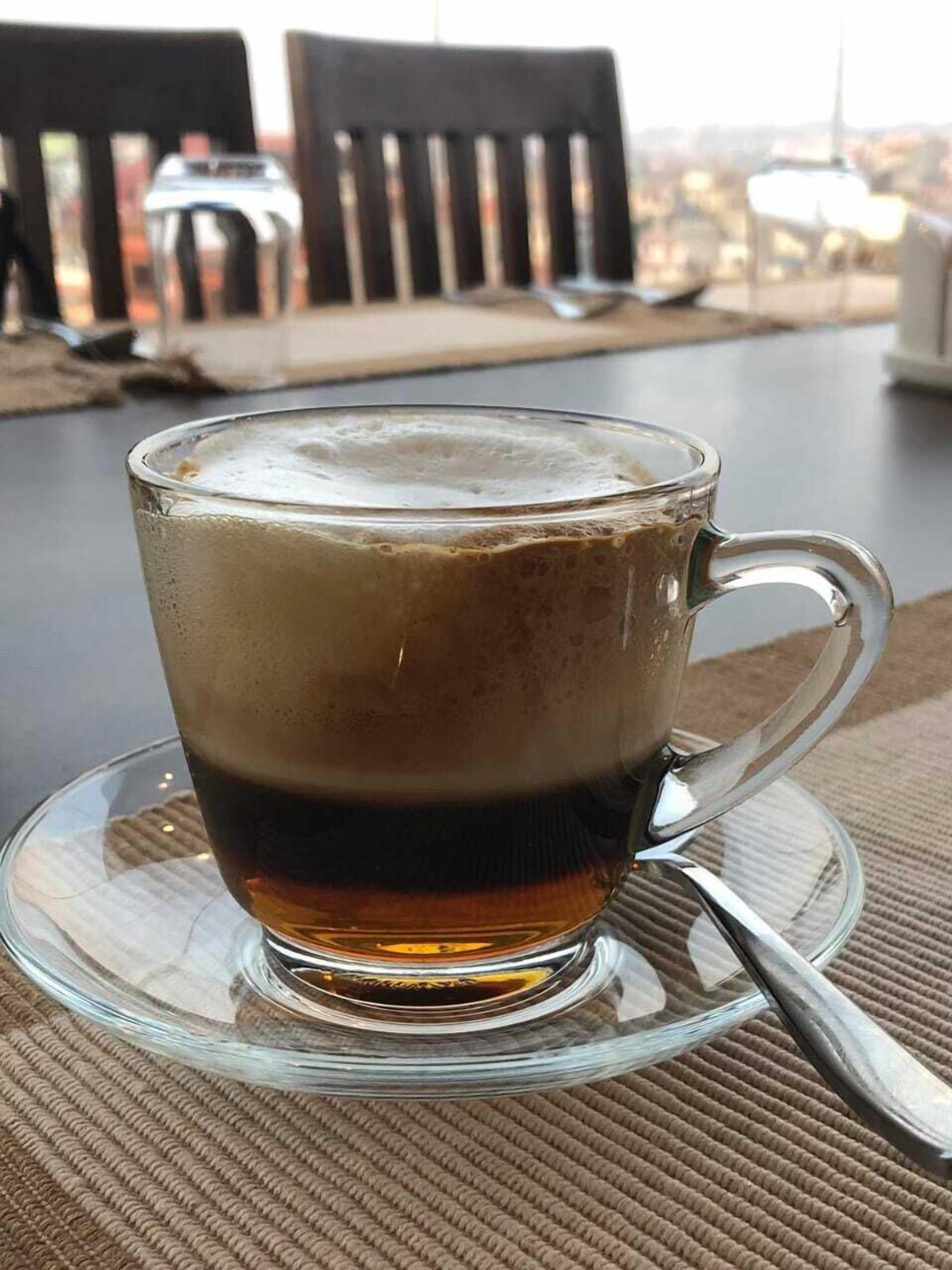 Une tasse à café en verre, posée sur une soucoupe avec une cuillère, le tout placé sur une surface texturée.