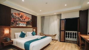 Habitación de hotel con una cama grande, un escritorio, una silla, un televisor y un cuadro en la pared.