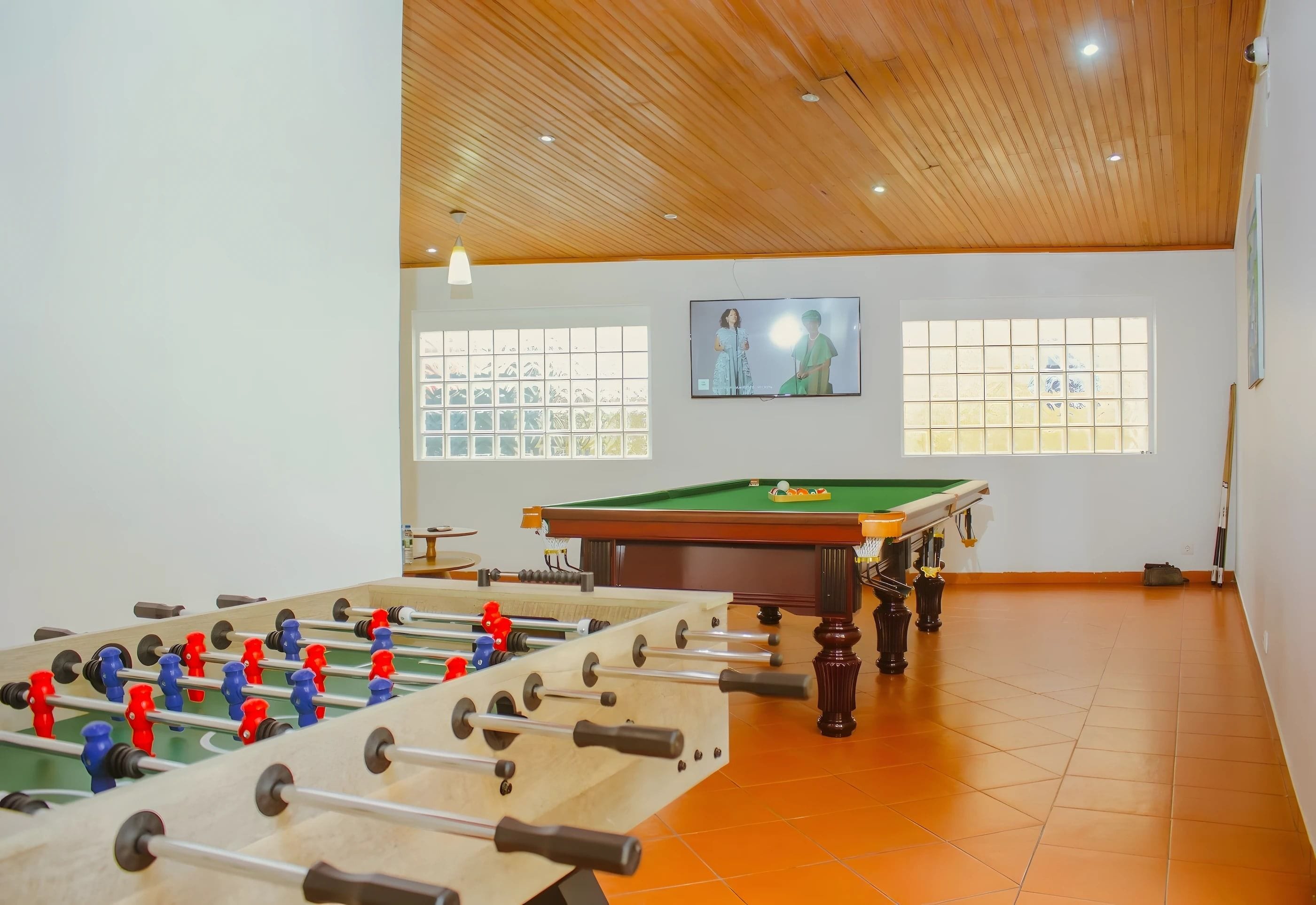 Una habitación con mesa de futbolín, mesa de billar y televisor mostrando un programa.