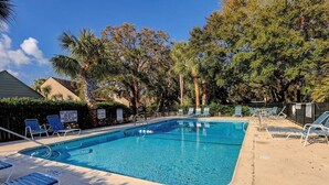 A rectangular swimming pool with clear blue water, surrounded by lounge chairs and palm trees.