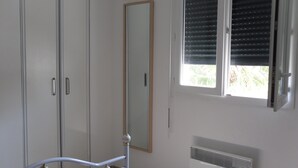 Un dormitorio con cama, armario, ventana con persianas y radiador.