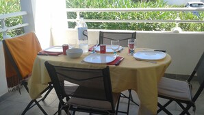 Mesa para dos en un balcón con mantel amarillo, dos sillas y una botella de agua.