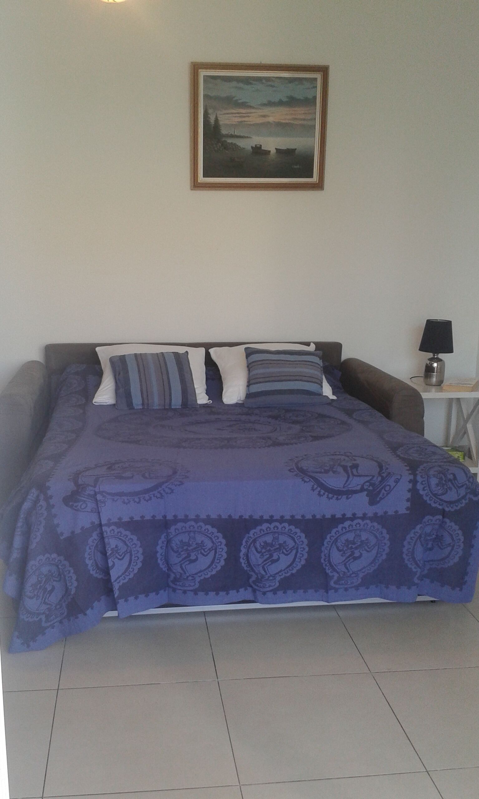 A bedroom with a bed, pillows, a nightstand, a lamp, and a painting on the wall.