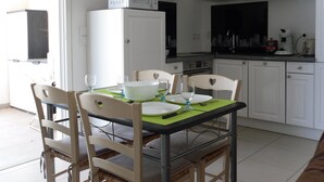 Cocina compacta con armarios blancos, microondas y estufa. Hay una mesa de comedor con sillas y un mantel individual verde.