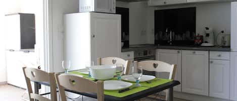 A compact kitchen with white cabinets, a microwave, and a stove. There is a dining table with chairs and a green placemat.
