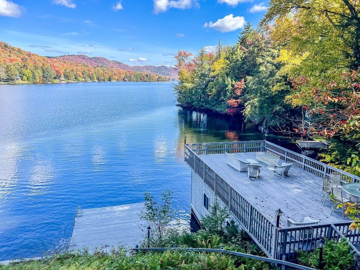 Eine Steg mit Außenbestuhlung mit Blick auf einen stillen See, umgeben von Herbstlaub.