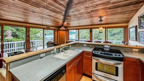 A kitchen with wooden ceiling, large windows, a built-in oven, and a dishwasher.
