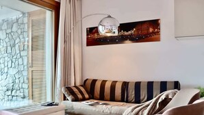A living room with a sofa, a bench, a lamp, and a cityscape painting.