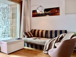 Un salon avec un canapé, un banc, une lampe et un tableau représentant un paysage urbain.