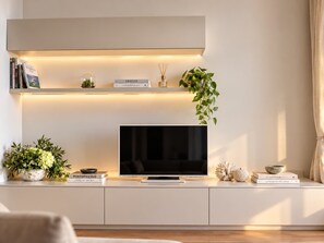 Ein modernes Wohnzimmer mit Fernseher, Büchern, Zimmerpflanzen und einem Regal mit Büchern und einer kleinen Vase.
