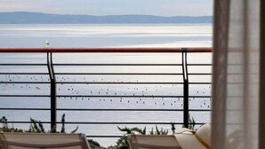 A balcony with a view of a calm sea and distant mountains.