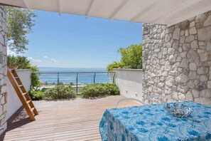 Un balcone con vista sul mare, un tavolo con tovaglia blu e un muro in pietra.