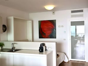 A modern kitchen with a sink, a camera on the counter, and a painting on the wall.