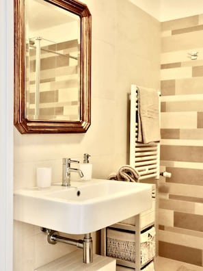Un bagno con un lavandino bianco, uno specchio con cornice in legno, un porta asciugamani e una cabina doccia.