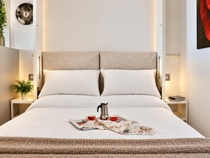 Un lit bien fait, avec une couette, des oreillers et un plateau contenant une bouilloire, une tasse et un journal.