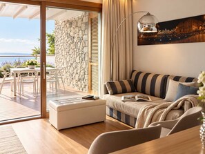 Un salon moderne avec un canapé, une table entourée de chaises, un mur en pierre et une vue sur la mer.
