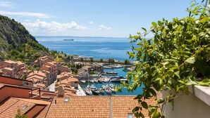A coastal town with terracotta-roofed buildings, a marina with boats, and a clear blue sea.