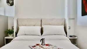 A neatly made bed with a tray of breakfast items, a clock on the wall, and a small plant on the nightstand.