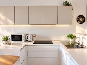 A modern kitchen with white cabinets, a microwave, a kettle, and a sink.