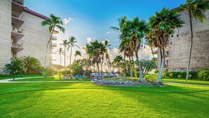 A well-maintained grassy area with palm trees and a brick building with balconies. - NEWLY Updated, Beachfront, WALK out to Beach, Pool, Hot Tub, BBQ! (Kihei)