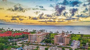 A coastal hotel with multiple buildings, a parking lot, and a view of the sea and sky. - NEWLY Updated, Beachfront, WALK out to Beach, Pool, Hot Tub, BBQ! (Kihei)