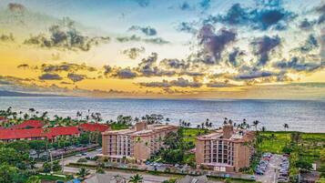 A coastal hotel with multiple buildings, a parking lot, and a view of the sea and sky.