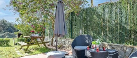 An outdoor patio area with wicker furniture, a picnic table, and a pergola with a grey umbrella.