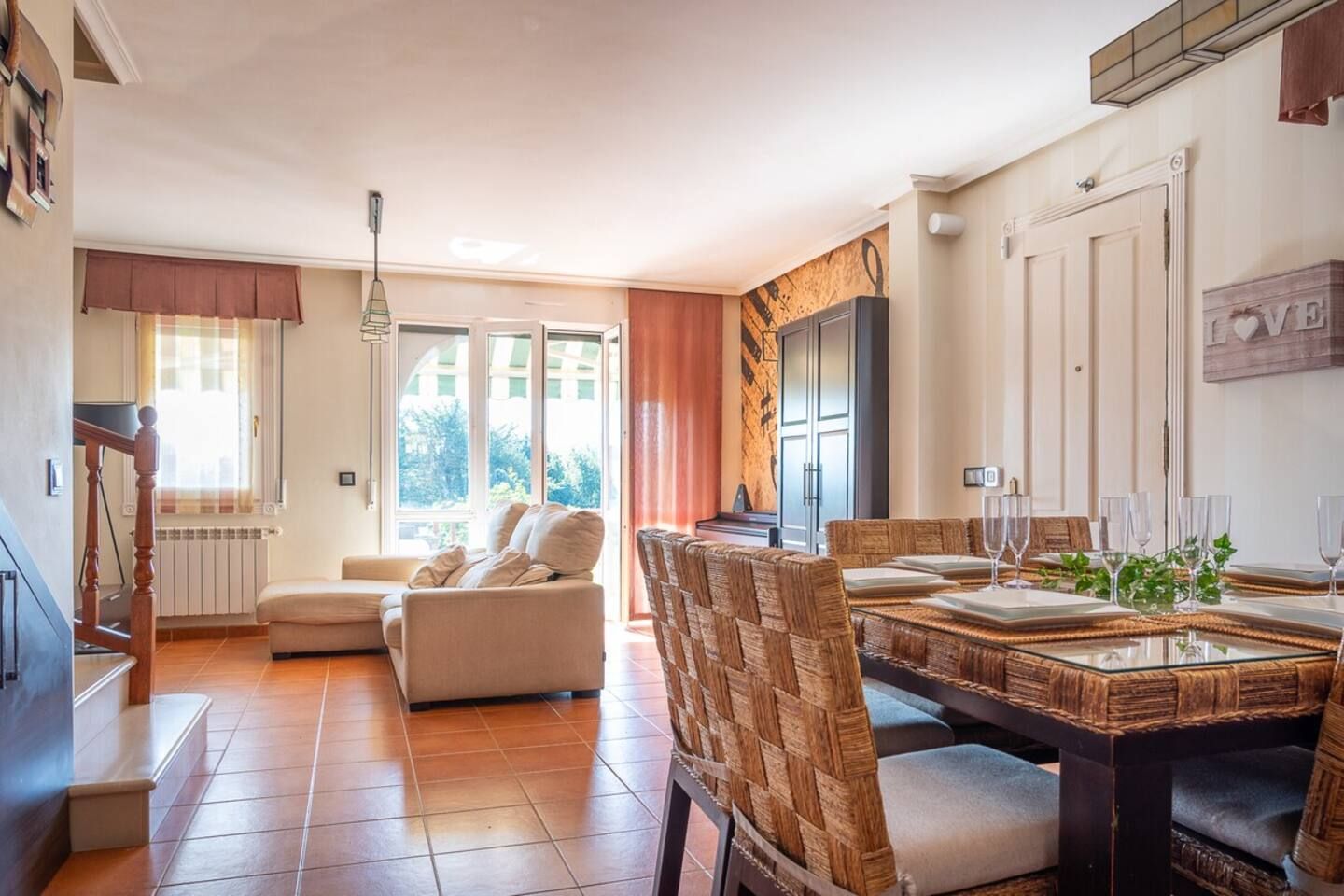 Een ruime woonkamer met een bank, eettafel en stoelen. Er is een keuken met kastjes en een koelkast.