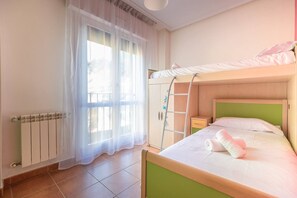 A bedroom with a bunk bed, a ladder, a radiator, and a window with sheer curtains.