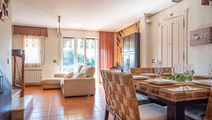 Un salón amplio con un sofá, una mesa de comedor servida con vasos y una escalera que sube a otro nivel.