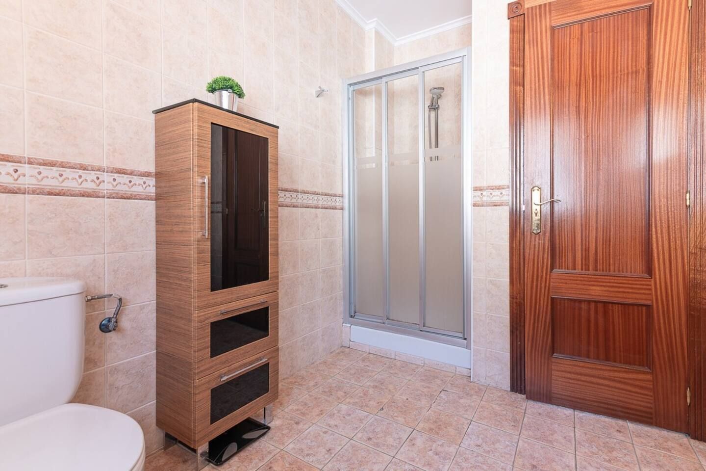 Une salle de bain comprenant des toilettes, un meuble en bois, une cabine de douche en verre et une porte en bois.
