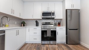 A modern kitchen with white cabinets, stainless steel appliances, and a wooden floor. - Sky Nook - Micro Studio - Pool, Hot Tub & Parking (Canmore)