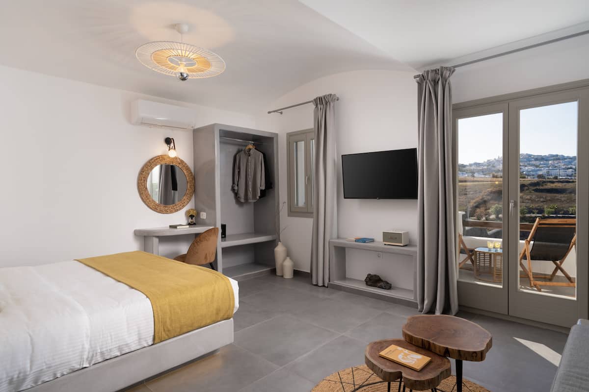 A modern hotel room with a bed, a TV, a desk, and a balcony with a view.