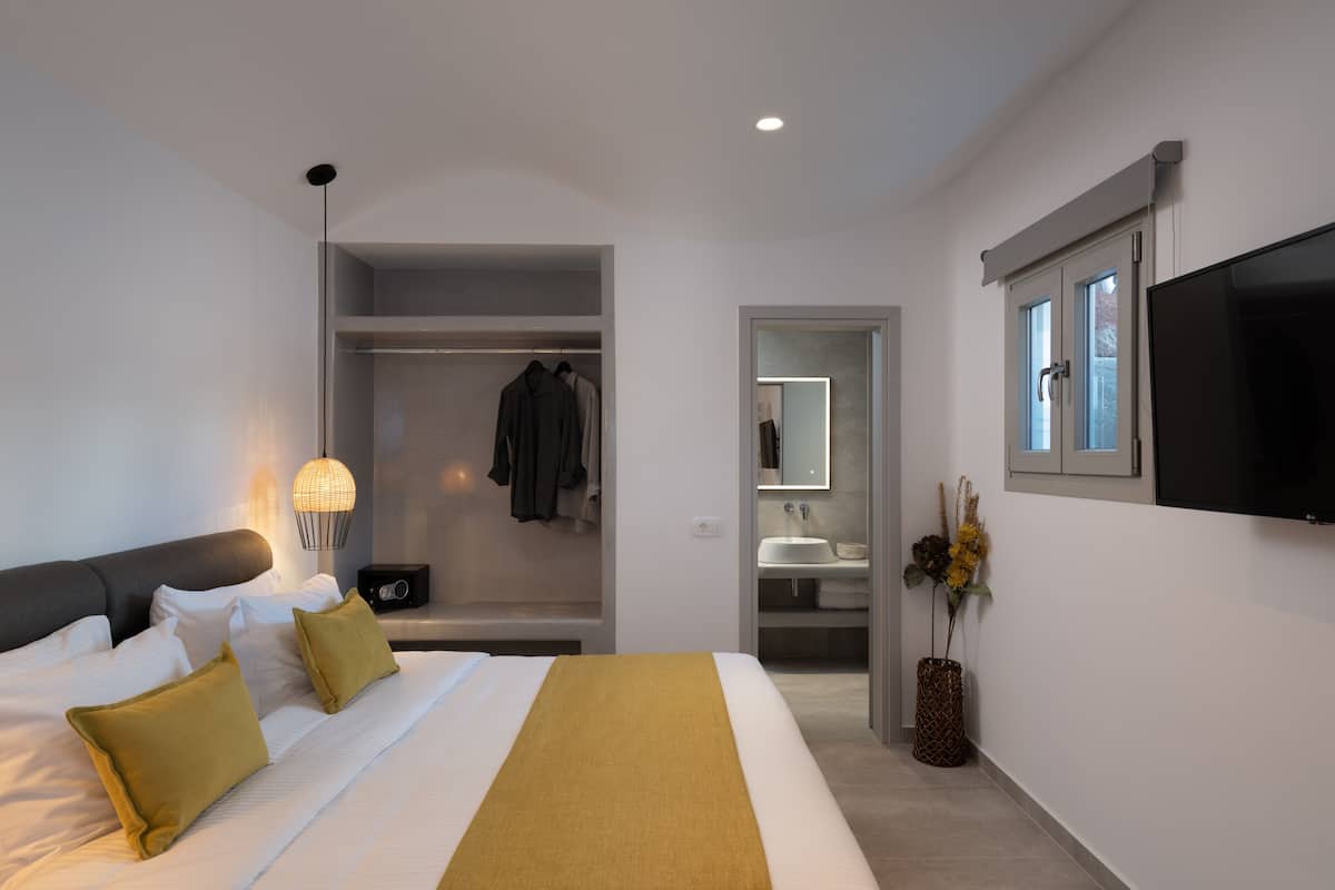A modern hotel room with a large bed, a walk-in closet, a bathroom with a mirror, and a TV mounted on the wall.