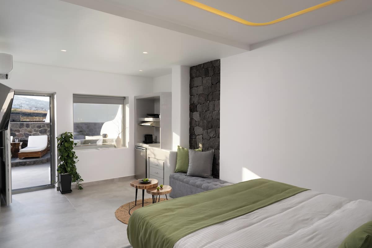 A modern bedroom with a large bed, a stone accent wall, a small desk, and a view of the outdoors.