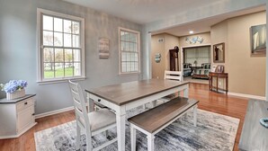 A spacious dining area with a wooden table and chairs, large windows, and a chandelier.