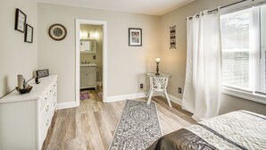 Une chambre à coucher comprenant un lit, une table de chevet, une commode, un tapis, un ventilateur de plafond et une fenêtre avec des rideaux.