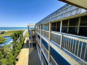 A multi-story building with balconies overlooking a beach, a pool, and a clear view of the ocean.