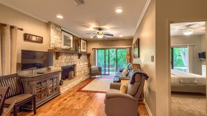 A spacious living room with a stone fireplace, a flat-screen TV, a comfortable sofa, and a ceiling fan.
