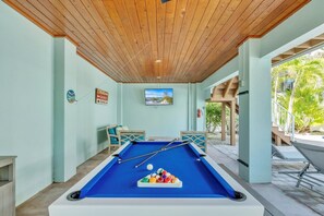 A pool table in a room with light green walls, wooden ceiling, and a television mounted above it. - Jersey Girl 5 Bedroom Home by RedAwning (Anna Maria)