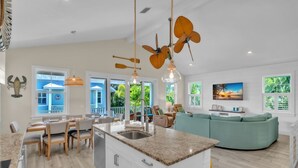 A spacious living area with a kitchen island, dining area, and a large window overlooking a blue building.