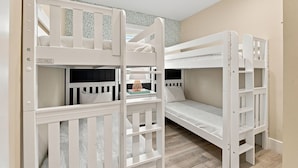 A room with bunk beds, a small table with a lamp, and patterned wallpaper.