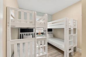 A room with bunk beds, a small table with a lamp, and patterned wallpaper. - Jersey Girl 5 Bedroom Home by RedAwning (Anna Maria)