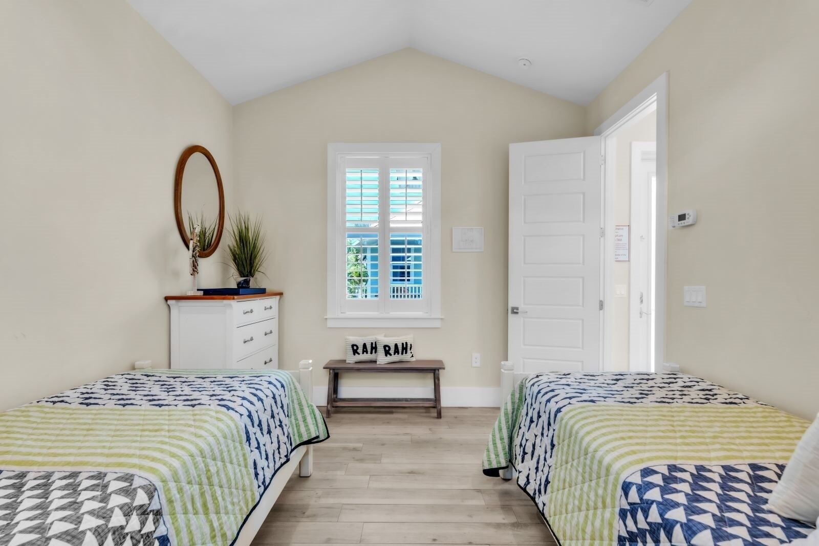 A bedroom with two beds, a dresser, a mirror, a window, and a door.