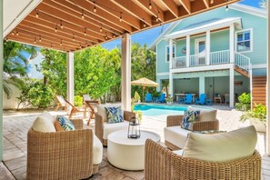 A covered outdoor seating area with wicker furniture, a pool, and a two-story building with a balcony. - Jersey Girl 5 Bedroom Home by RedAwning (Anna Maria)